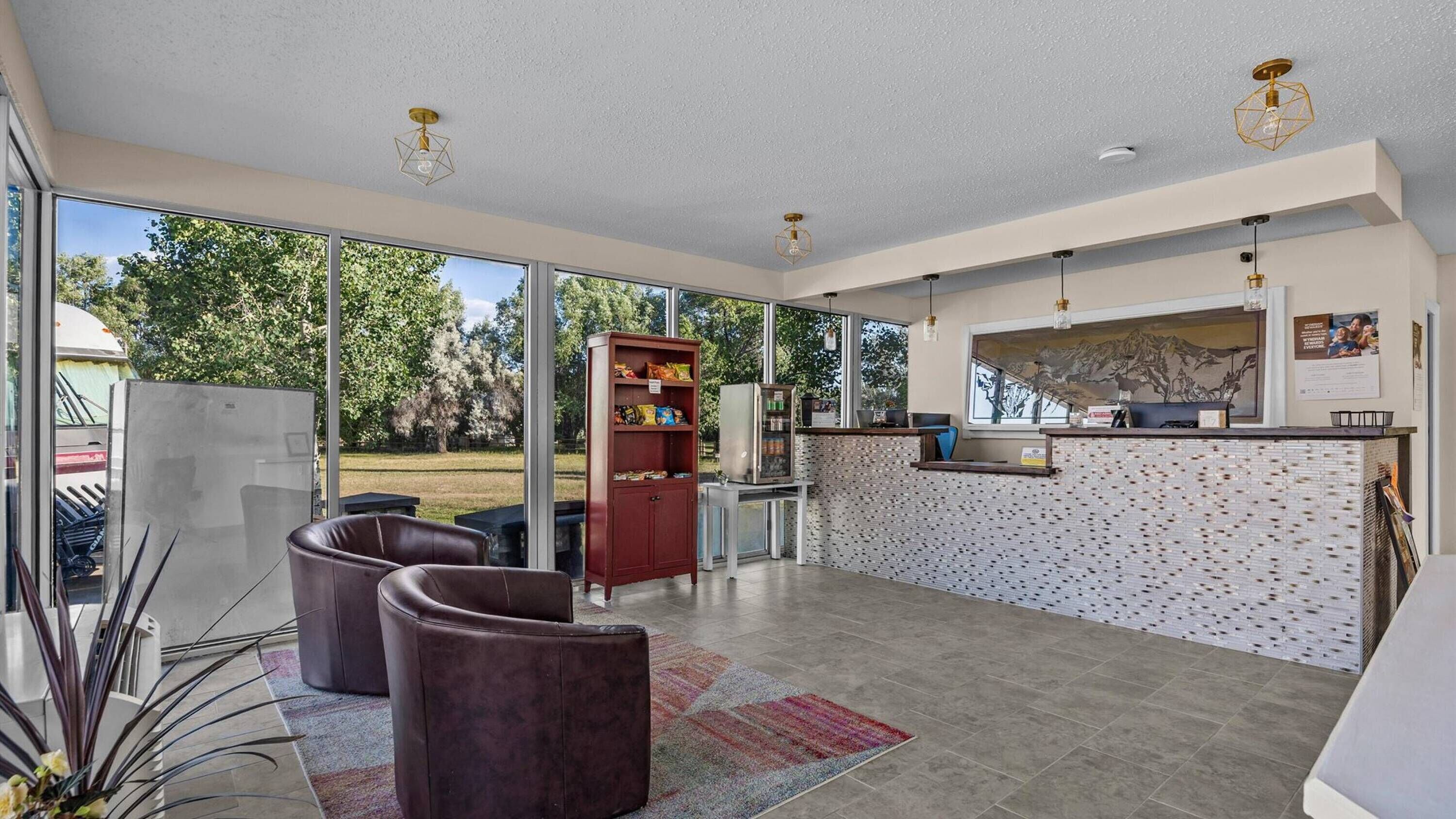 A spacious lobby with a reception desk, a seating area with leather chairs, a vending machine, and a large window offering a view of the outdoors.