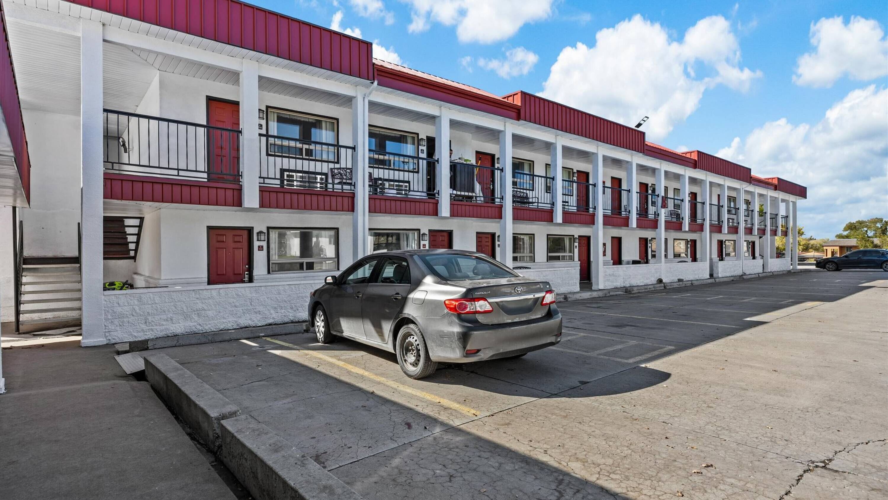 Un motel de varios pisos con fachada roja y blanca, un estacionamiento y un coche estacionado.