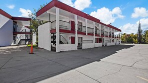 A multi-story motel with a red and white exterior, a covered parking area, and a visible staircase leading to the entrance.