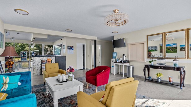 A spacious living room with a sofa, armchairs, a coffee table, and a TV. There is a kitchen area in the background with a water dispenser and a coffee machine. - Red Arrow Inn & Suites, a Travelodge by Wyndham (Montrose)