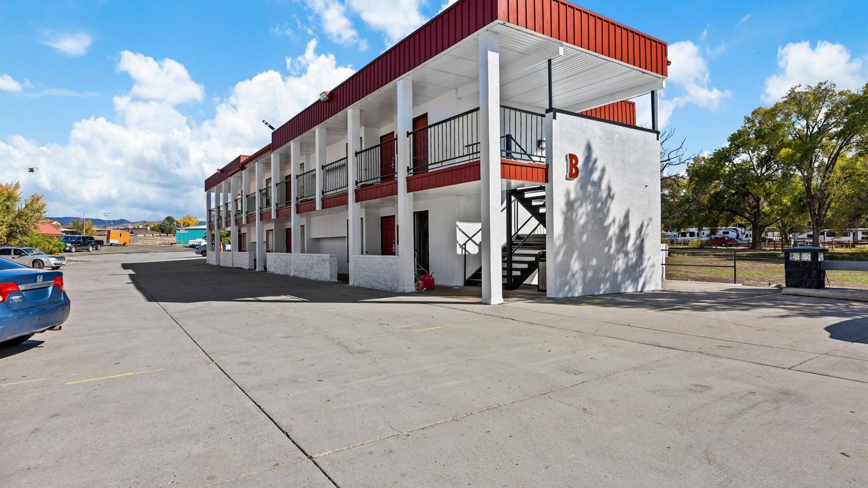 A motel with a red and white exterior, a covered parking area, and a staircase leading to the entrance.