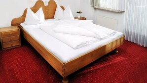 A neatly made bed with white linens, a wooden headboard, and two bedside tables with lamps. - Appartementhaus Alpina (Bad Hofgastein)