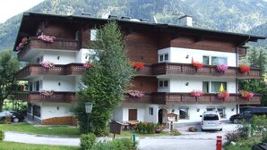 A multi-story building with balconies adorned with flowers, a sign reading "Alpina," and a car parked in front. - Appartementhaus Alpina (Bad Hofgastein)