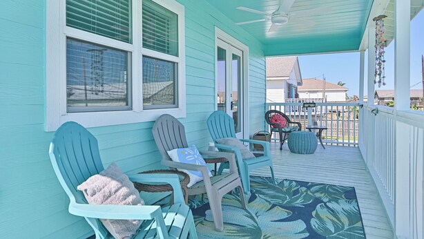 A covered porch with two Adirondack chairs, a small table, and a decorative hanging ornament. - Sea Shed-Big yard in Jamaica Beach-Pet Friendly! (Jamaica Beach)
