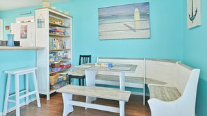 A room with a teal wall, a white bench, a white table, and a bookshelf filled with books and decorative items. - Sea Shed-Big yard in Jamaica Beach-Pet Friendly! (Jamaica Beach)