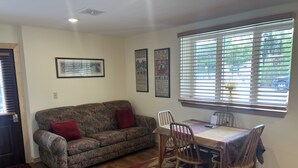 A living room with a sofa, a dining table with chairs, a window with blinds, and a door with a window. - ADULTS 25 and older, Creekside Vacation Rental Suite 2,  Downtown, CITY APPROVE (Buffalo)