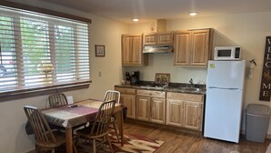 A kitchen with wooden cabinets, a refrigerator, a microwave, a sink, and a dining area with chairs and a table. - ADULTS 25 and older, Creekside Vacation Rental Suite 2,  Downtown, CITY APPROVE (Buffalo)