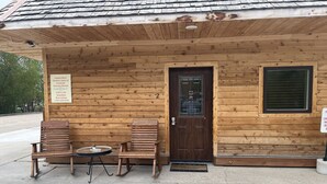 A wooden cabin with a porch, two rocking chairs, a small table, and a door with a window. A sign on the wall advertises vacation rentals. - ADULTS 25 and older, Creekside Vacation Rental Suite 2,  Downtown, CITY APPROVE (Buffalo)