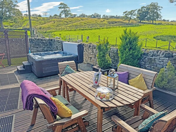 A wooden deck with a hot tub, outdoor seating, and a scenic view of a green field.