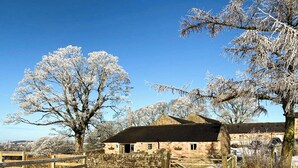 Un bâtiment rustique en pierre, doté d’un portail en bois, entouré d’arbres couverts de neige.
