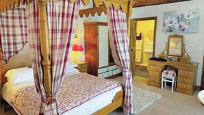 Une chambre à coucher avec un lit à baldaquin, une commode en bois, une coiffeuse avec un miroir et un petit tabouret.