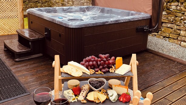 Un bain à remous avec des marches, entouré d’une terrasse en bois, et une planche de fromages et de vins posée devant.