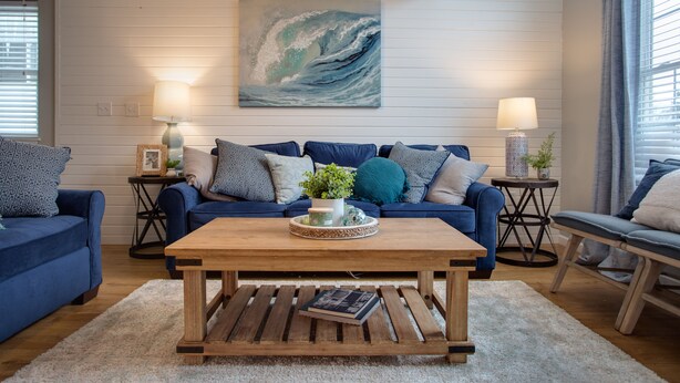 A living room with a blue sofa set, a wooden coffee table, and a large wave painting on the wall. - Lake Erie Getaway Near The Beach & Cedar Point (Huron,)