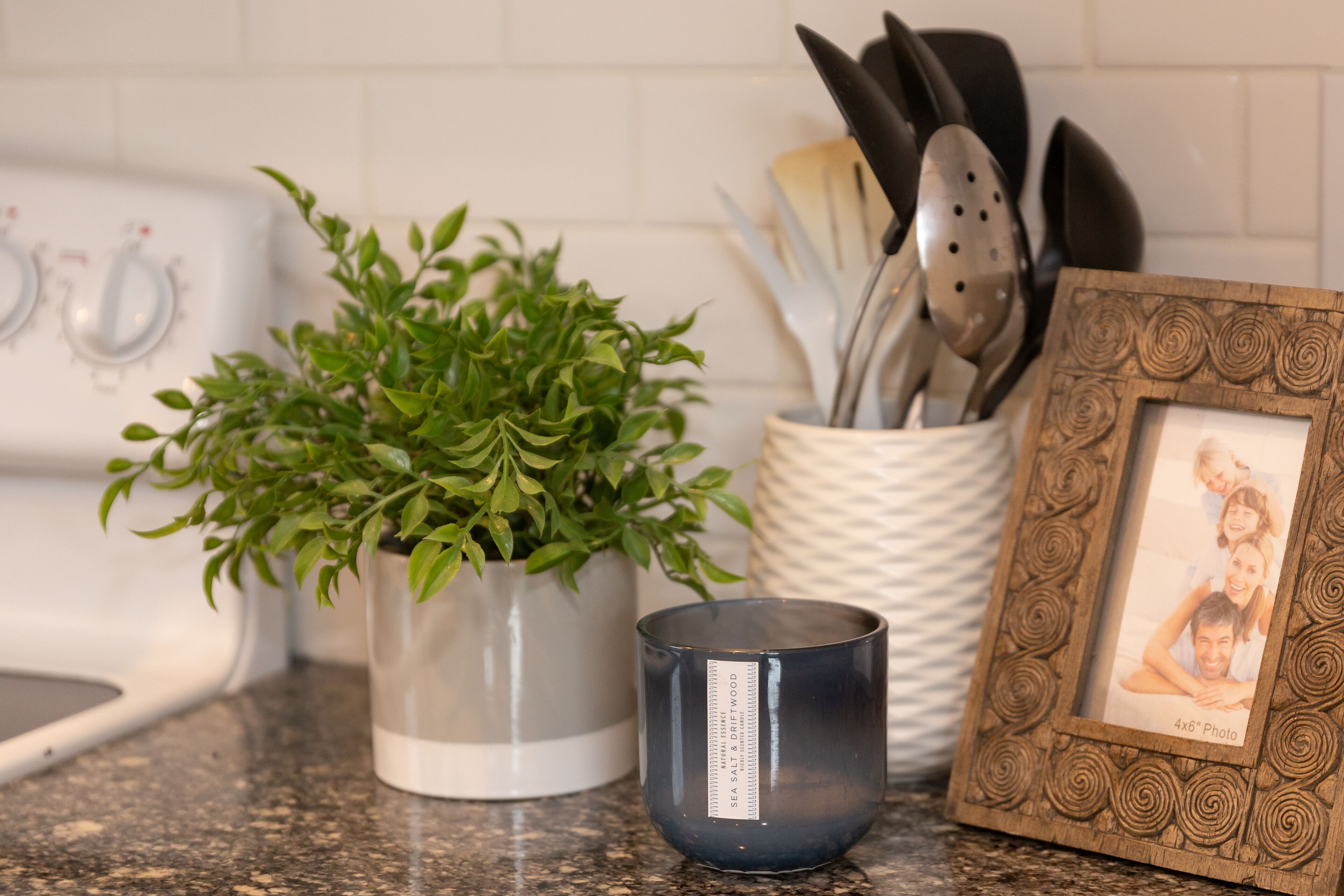 A kitchen counter with a potted plant, a candle, a picture frame, and kitchen utensils.