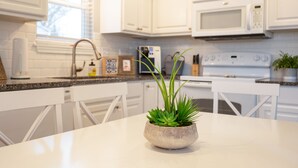 A modern kitchen with white cabinets, a granite countertop, a white stove, and a potted plant on the table. - Lake Erie Getaway Near The Beach & Cedar Point (Huron,)
