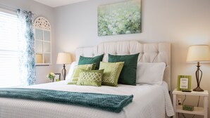 A neatly made bed with a quilted white duvet, two green pillows, and a teal throw blanket. There is a white bedside table with a lamp and a framed picture. - Lake Erie Getaway Near The Beach & Cedar Point (Huron,)