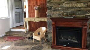 A stone fireplace with a wooden mantel, a wicker chair, and a small table with a vase of flowers. - Air Bellows Gap Retreat (Sparta)