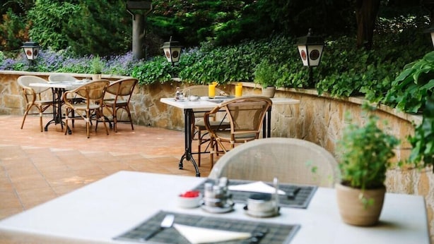 An outdoor patio area with stone flooring, wicker chairs, and tables set for dining. - Mediterran Hotel (Budapest)