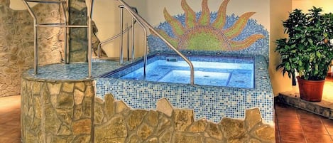 A hot tub with mosaic tiles, a stone wall, and a metal staircase.
