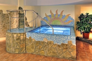 A hot tub with mosaic tiles, a stone wall, and a metal staircase. - Mediterran Hotel (Budapest)