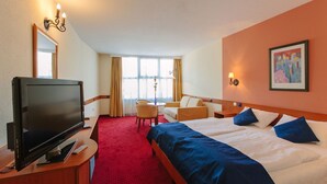 A hotel room with a bed, a TV, a desk, a chair, and a window with curtains. - Mediterran Hotel (Budapest)