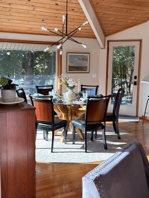 Un espace repas comprenant une table ronde, des chaises, un lustre et une vue dégagée grâce à de grandes fenêtres.