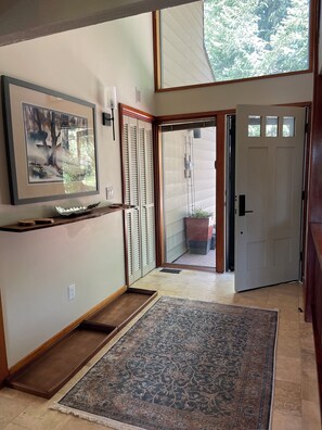 A hallway with a large framed picture, a wooden bench, a patterned rug, a sliding glass door, and a door with windows.