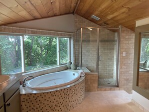 A bathroom with a large bathtub, a glass-enclosed shower, and a view of the forest through large windows. - Browne’s Mtn Retreat, South Hill Views and Hot Tub (Spokane)