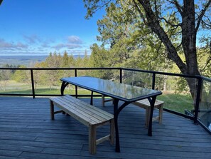 A wooden deck with a table and bench, overlooking a scenic landscape with trees and distant hills. - Browne’s Mtn Retreat, South Hill Views and Hot Tub (Spokane)