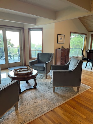 A spacious living room with a large window, a wooden coffee table, two armchairs, and a cabinet.