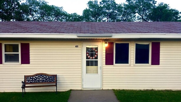 A single-story house with a front door, a bench, and a number 411 on the wall.