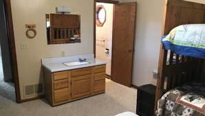 A bedroom with a bunk bed, a wooden cabinet with a mirror, a white sink, and a door leading to another room.