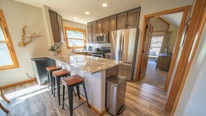 A modern kitchen with wooden cabinets, stainless steel appliances, and a granite island with bar stools. - Snake River 1 (Keystone)