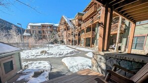 A wooden deck with benches, a stone wall, and a snow-covered landscape with buildings in the background. - Tenderfoot Lodge 2611 (Keystone)