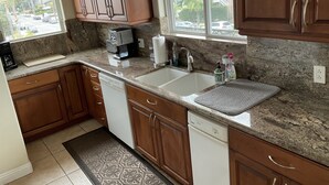 A kitchen with wooden cabinets, a coffee maker, a dishwasher, and a window with a view of palm trees and a street. - Carlsbad Village, Great Beach Access, Shops & Restaurants (Carlsbad)