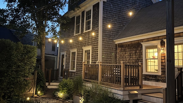 Une maison à deux étages avec un porche à l’avant, un chemin de gravier et des guirlandes lumineuses.