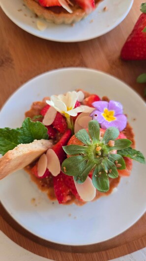 Une assiette contenant un dessert garni de fraises, de fleurs et de feuilles de menthe.