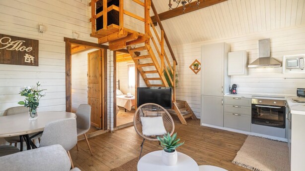 A loft-style room with a wooden staircase, a dining area with a table and chairs, a kitchen with modern appliances, and a cozy seating area with a chair and a plant. - Rural las Bodegas Setenil de las Bodegas by Ruralidays (Cádiz)