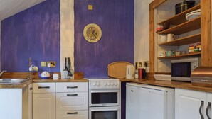 A kitchen with white cabinets, a stove, oven, microwave, and a wooden chair. - 3 bedroom accommodation in Welton (Welton)