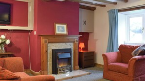 A living room with a fireplace, red walls, wooden beams, a television, and a sofa. - 3 bedroom accommodation in Welton (Welton)