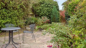 A patio with a round table and two chairs, surrounded by dense foliage and a variety of plants. - 3 bedroom accommodation in Welton (Welton)