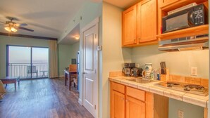 A spacious living area with a balcony, a kitchen with wooden cabinets and modern appliances, and a dining area with a table and chairs. - Origin 1020 | Rare Gulf-Front Studio w/ Unobstructed Views + Free Activities! (Panama City Beach)