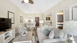 A modern living room with a television, sofa, and dining area. - Origin 1208: Gulf-View 1BR w/ Balcony & Washer/Dryer! (Panama City Beach)
