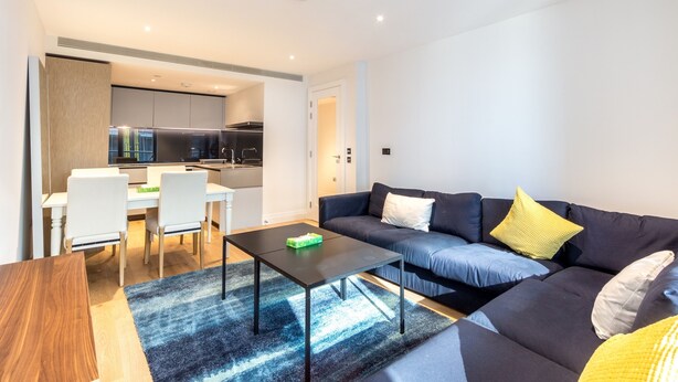 A modern living room with a dark sofa, a coffee table, and a dining area with chairs and a table.