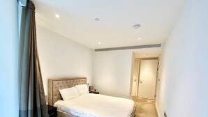 A bedroom with a large bed, a nightstand, a dresser, and a door leading to another room.