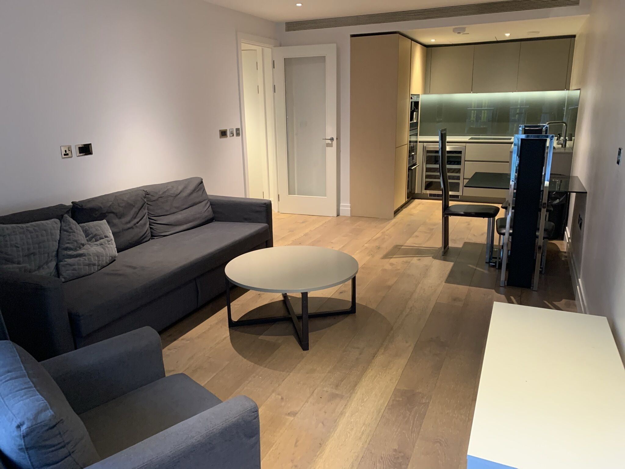 Un salon moderne avec un canapé gris, une table basse ronde et un coin repas comprenant une table et des chaises blanches.