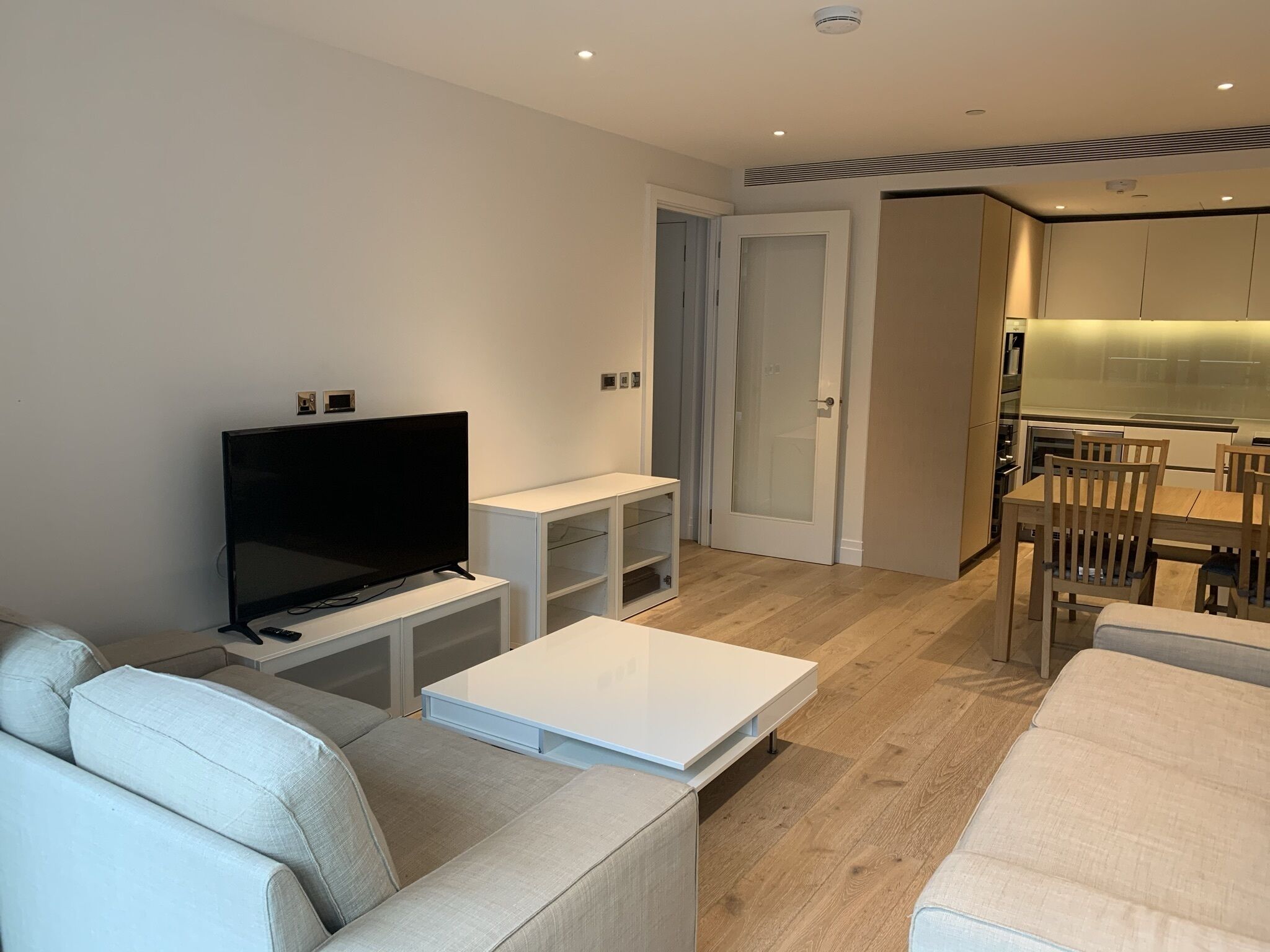 A modern living room with a flat-screen TV, a white coffee table, and a sofa.