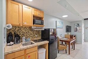 A kitchen with wooden cabinets, a microwave, a stove, and a refrigerator. There is a dining table with chairs and a trash can. - Origin 1323 | Steps to Beach + Free Activities! (Panama City Beach)