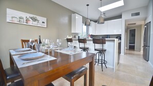 A modern kitchen with white cabinets, a dining area with a wooden table and chairs, and pendant lighting.