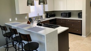 A modern kitchen with a central island, bar stools, a microwave, and a coffee maker.